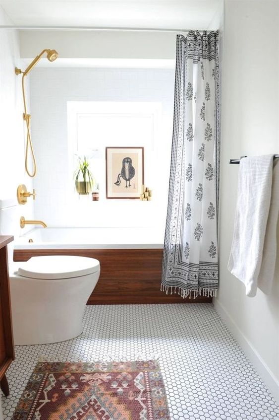 a modern small bathroom with a penny tile floor, a wood clad bathtub, a rug, an artwork and gilded touches