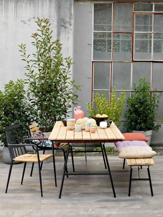 a modern spring terrace with a simple and chic dining set, potted greenery and bright pillows is a fun and cool idea