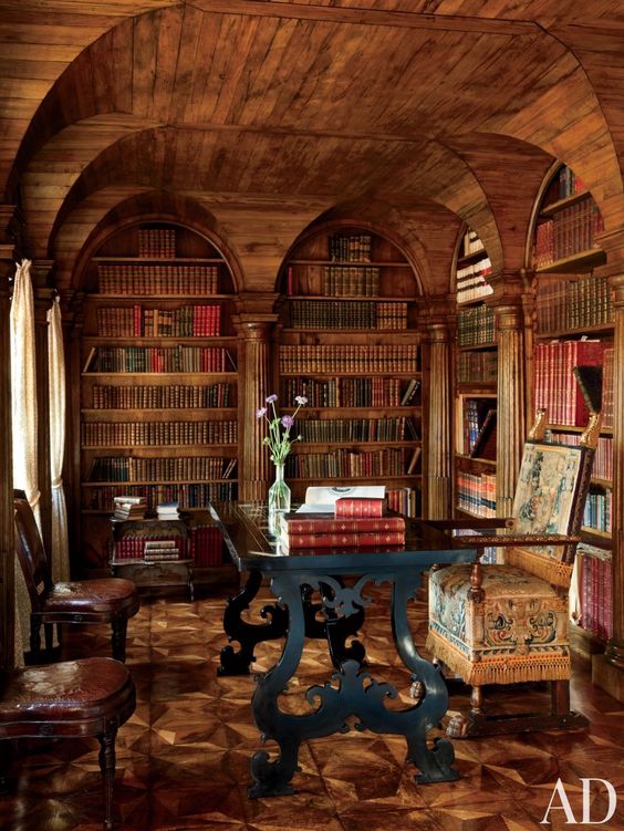 a moody Gothic library and home office with an arched ceiling, a black carved desk, heavy chairs is a beautiful example of Gothic style