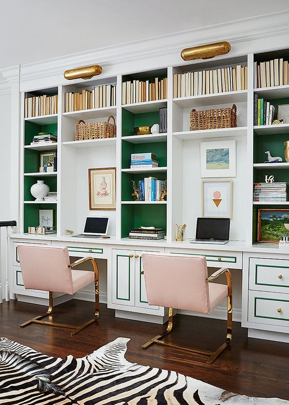 A refined home office with built in bookshelves with green backing and pink metallic chairs and a faux zebra rug