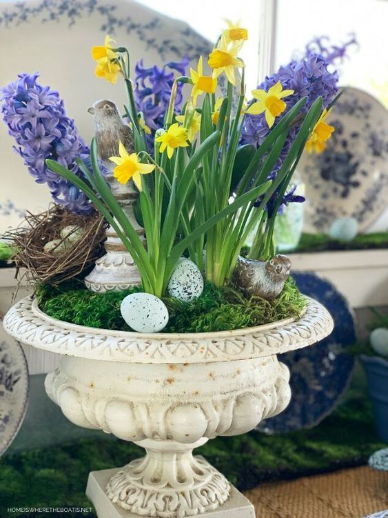a refined spring decoration of a vintage urn with moss, daffodils and hyacinths, fake eggs, nests and birds