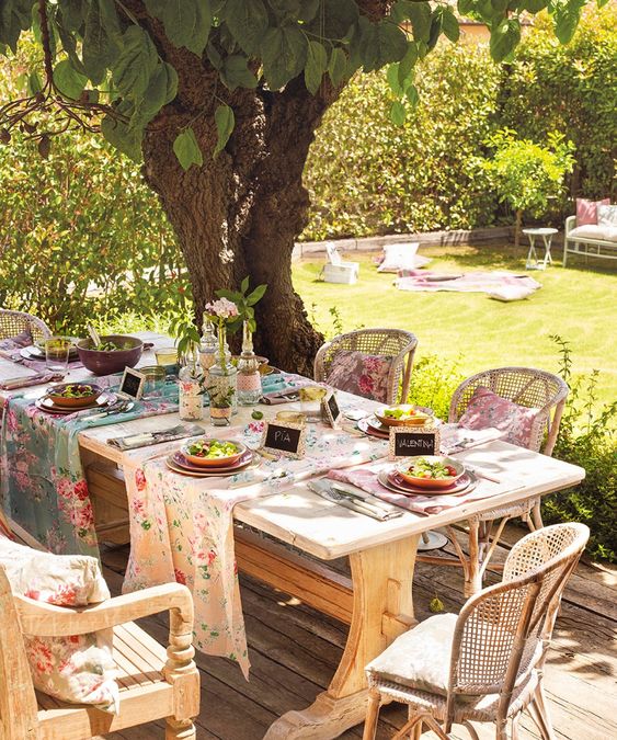 a rustic spring terrace with a wooden table and wicker chairs, with floral runners and napkins set for a party