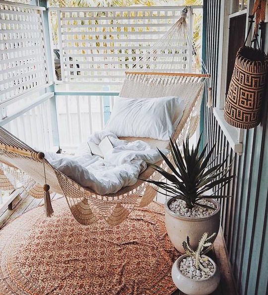 a screened boho porch with a macrame hammock with neutral linens, a printed rug, potted plants is a cool space