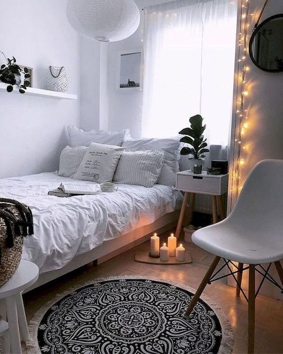 a small Scandinavian bedroom with white walls and furniture, lights, candles and pendant lamps