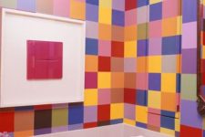 a small and colorful powder room with super bright tiles all over it, a red cabinet and a free-standing sink plus a bold artwork