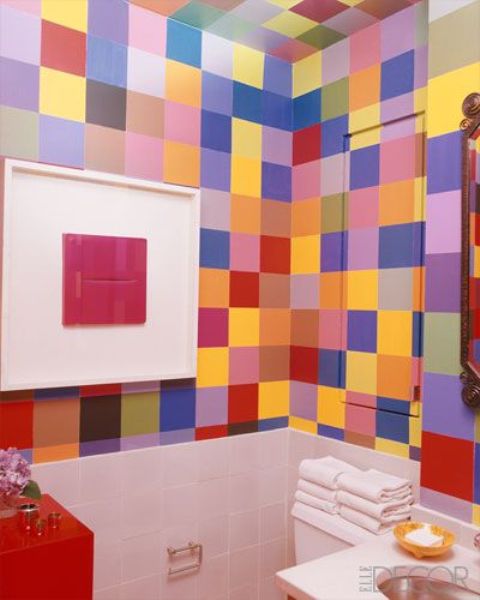 A small and colorful powder room with super bright tiles all over it, a red cabinet and a free standing sink plus a bold artwork