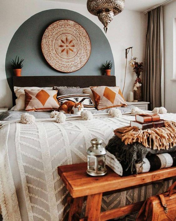 a small boho bedroom with a black bed, a Moroccan lamp, a wooden bench and potted plants here and there