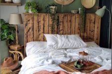 a small boho bedroom with a green wall, a pallet bed, a gallery wall, some lamps and potted greenery and catchy textiles