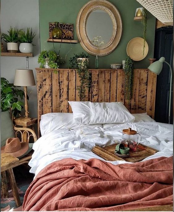 a small boho bedroom with a green wall, a pallet bed, a gallery wall, some lamps and potted greenery and catchy textiles