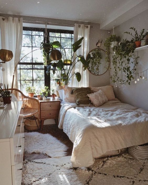 a small boho bedroom with cascading greenery in pots, wooden furniture and brass lamps