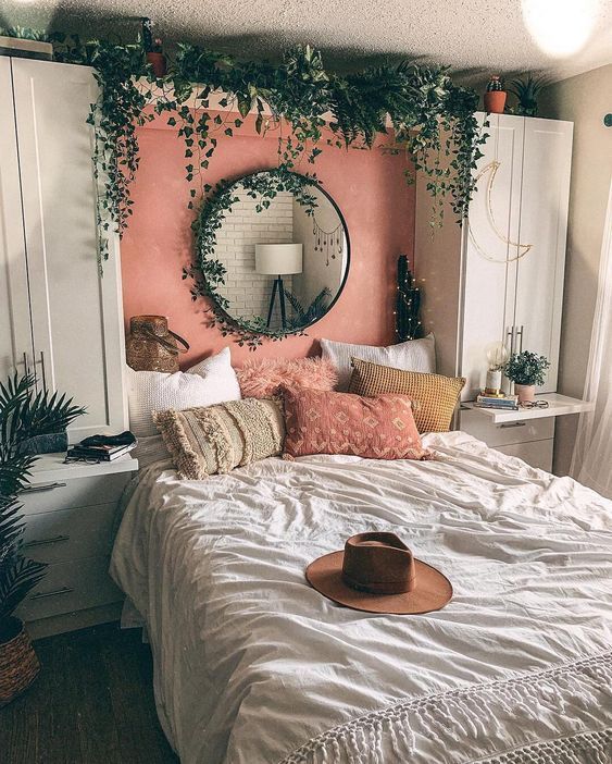 A small boho bedroom with white wardrobes and a built in bed, lots of cascading greenery, boho pillows and lights