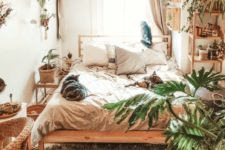 a small boho bedroom with wooden and wicker furniture, potted greenery, neutral textiles is flooded with light