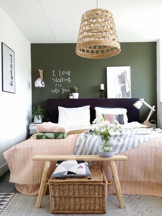 a small catchy bedroom with a green accent wall, a black bed, a wicker lamp and chest and printed textiles