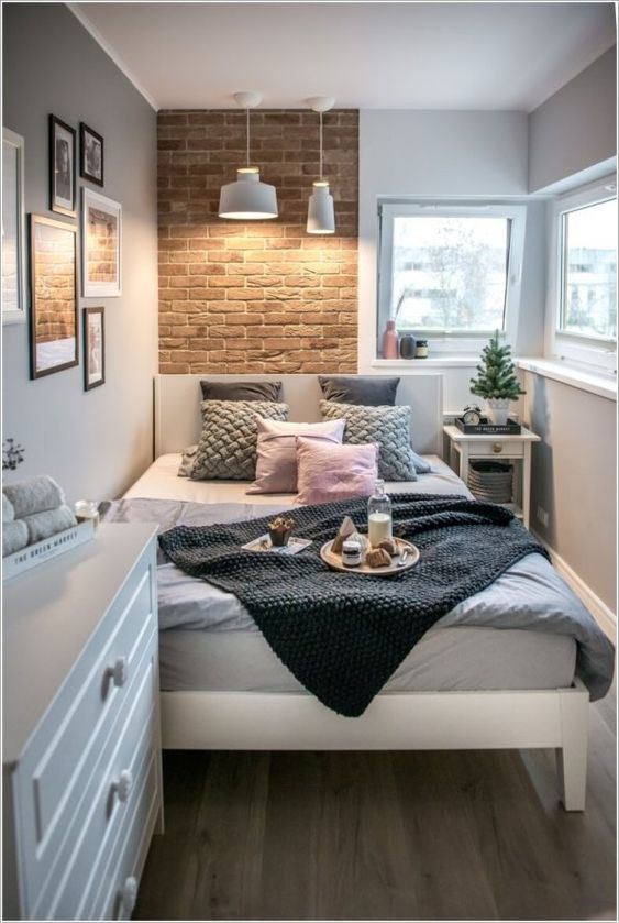 a small contemporary bedroom with a brick wall, a white bed and dresser, pendant lamps and catchy bedding