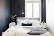a small modern bedroom with black and white walls, a grey bed, leather stools and lamps and bulbs