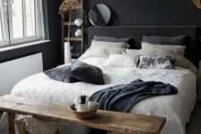 a small moody bedroom with black walls and a bed, with a wooden bench and ladder, pendant lamps