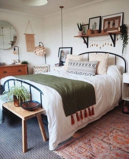 a spring boho bedroom in neutrals, with a metal bed, wooden furniture, macrame, potted greenery and printed bedding