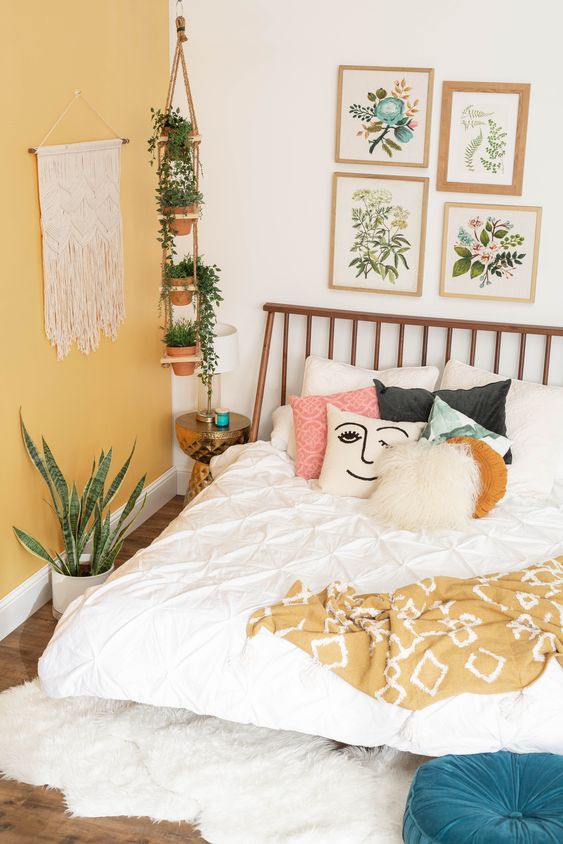 a spring boho bedroom with a yellow statement wall, printed bedding, a floral gallery wall and potted plants