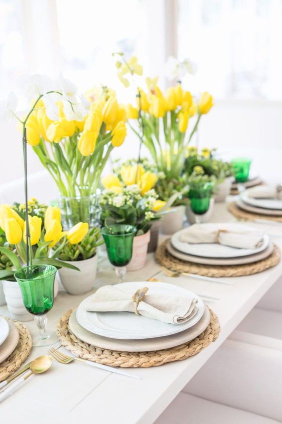 A spring tablescape with bright yellow tulips, fresh greenery and green glasses looks bold, fresh and very spring like