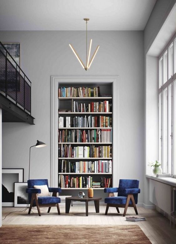 A stylish conversation and reading nook with navy velvet chairs, a large built in bookshelf unit and a cool chandelier