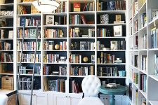 a stylish home office and library in one with built-in bookshelves, a white chair, a pendant lamp and some vintage items