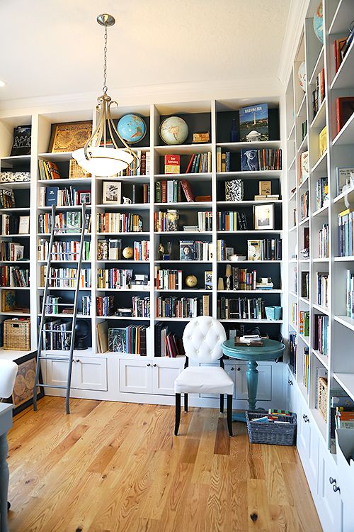 a stylish home office and library in one with built-in bookshelves, a white chair, a pendant lamp and some vintage items