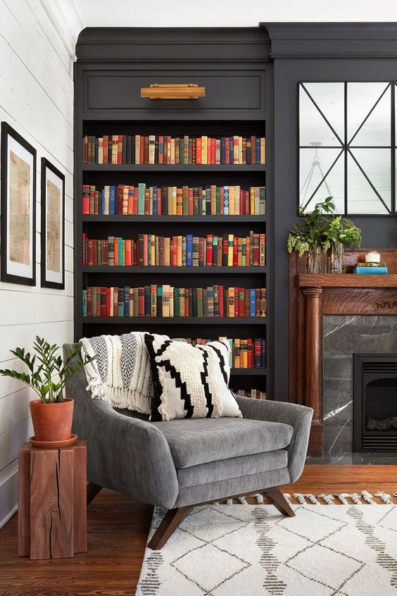A stylish moody space with dark built in bookshelves, a marble fireplace and a grey chair for much comfort