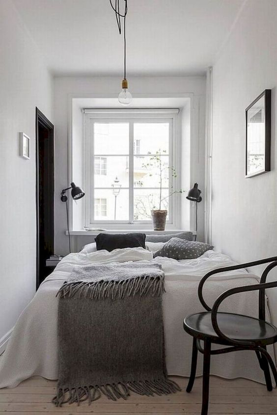 a tiny Scandinavian bedroom with black sconces, a black chair and a bed with comfy bedding