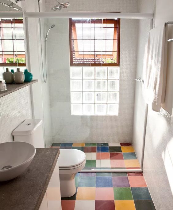 A tiny modern bathroom with a multi color tile floor, white appliances and a vanity with a stone countertop, a window for natural light
