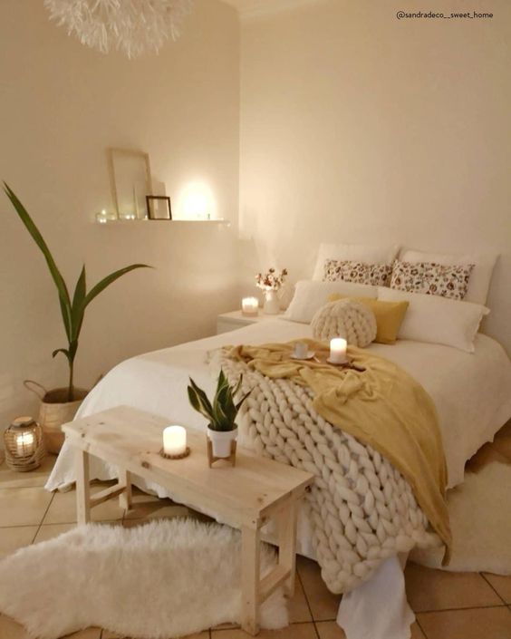 a tiny neutral bedroom with catchy bedding and a chunky knit blanket, a wooden bench, potted greenery and candles