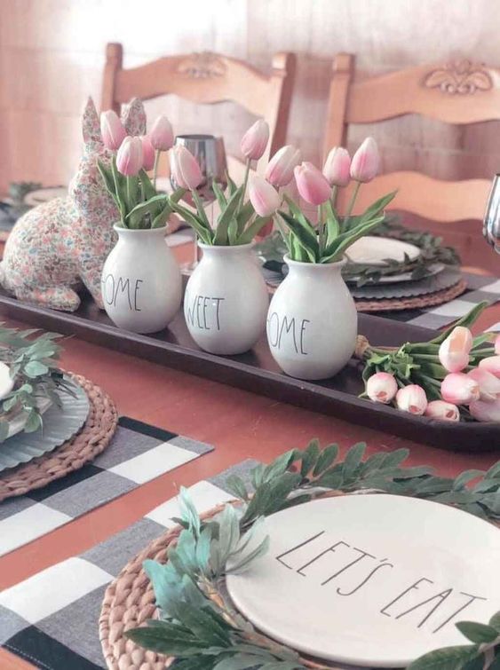 A tray with a floral bunny, pink tulips in vases and greenery wreaths for each place setting feel spring like