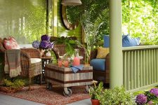 a tropical boho porch with woven furniture, a wooden coffee table, potted greenery and colorful textiles