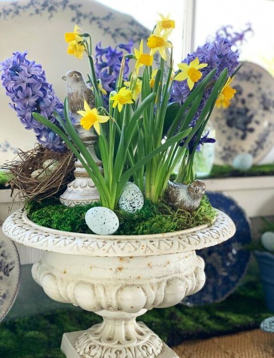a vintage urn with moss, fake eggs and a nest, purple hyacinths and yellow daffodils for a rustic feel and a spring touch