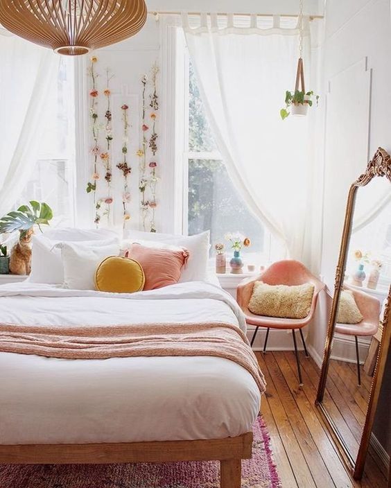 a warm spring bedroom with a wooden bed, a pink chair, pink and yellow pillows, faux blooms attached to the wall