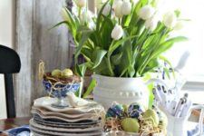 a wicker tray with blue linens, a nest with eggs and a bowl with them and a jar with white tulips for a spring and Easter look