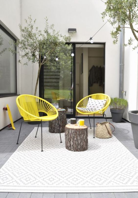 an eclectic spring terrace with neon yellow chairs, tree stumps, potted greenery and plants and printed pillows