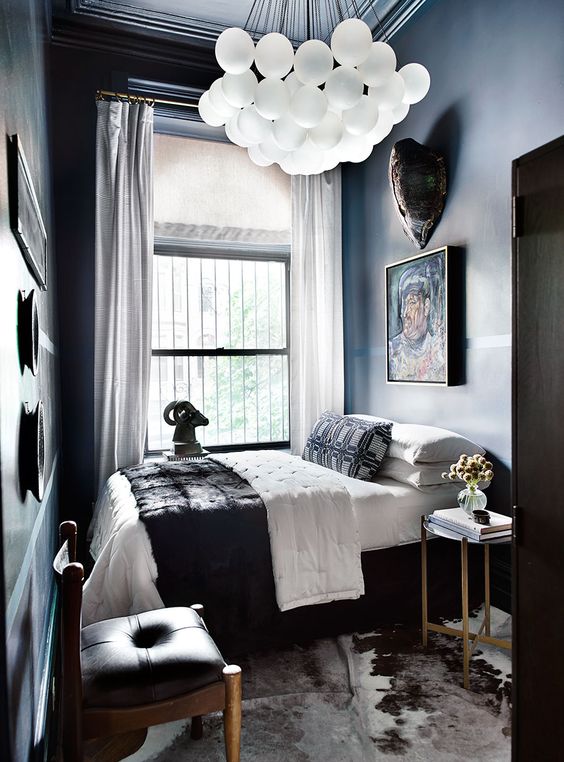 an elegant moody bedroom with dark walls, a catchy chandelier, artworks, an animal rug and leather chairs