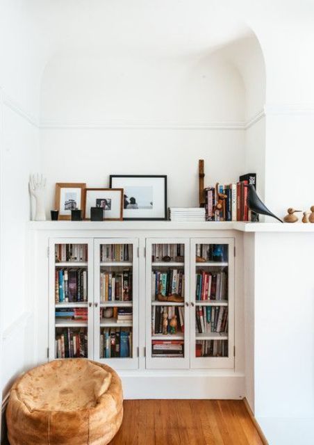 Built in bookshelf units with glass doors and a small pouf for a cozy reading nook