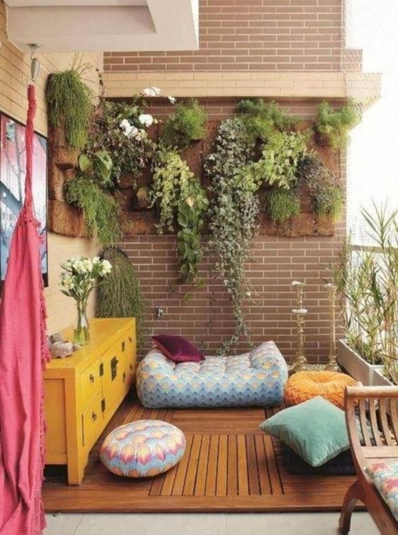 colorful cushions and pillows, a bright chest, a blanket and some greenery in pots on the wall