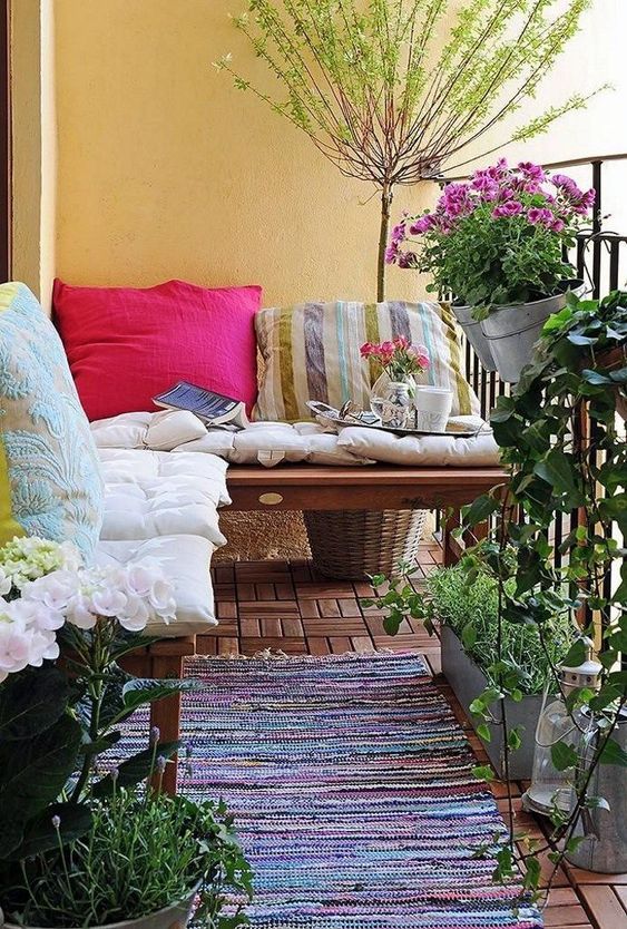 Colorful pillows and a boho rug, potted greenery and flowers are bold and cool for a rustic like balcony