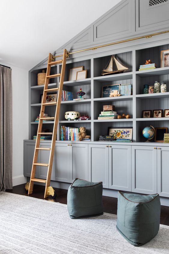 Grey built in bookshelves, blue poufs and a ladder to get all the books comfortably
