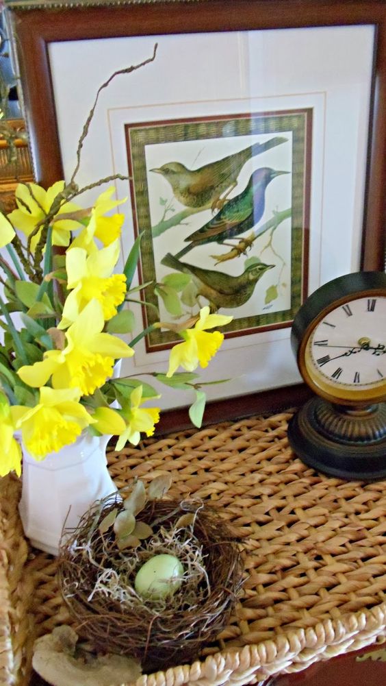 spring home decor with a faux nest and eggs, a white jug with daffodils, a bird print and a clock is refined and chic