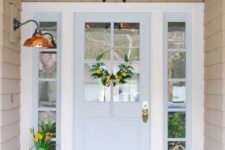 stylish spring porch decor with a watering can, candle lanterns, bright blooms in pots and a bright yellow wreath