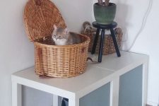 two IKEA Lack tables with paper covers, a cat litter box under them and a basket cat bed on top