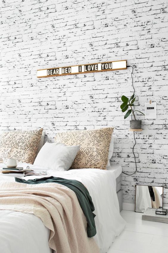 a Nordic bedroom with a whitewashed brick wall, a grey bed, lights and plants is a stylish and welcoming space