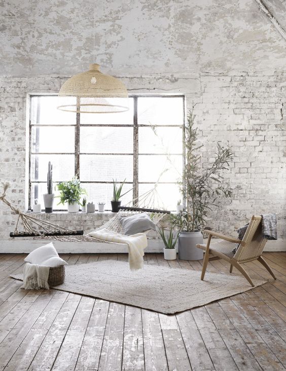 a Nordic living room with whitewashed brick walls, a hammock, a woven chair, a pendant lamp and some pillows