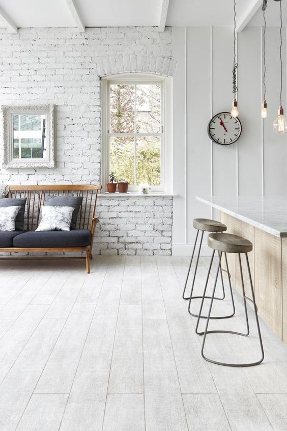 a Nordic space with whitewashed brick walls, a wooden floor, a bar space with stools and a loveseat