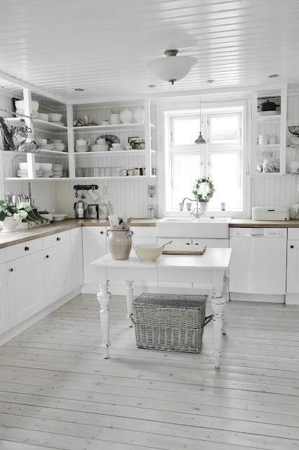 a Scandinavian kitchen with white beadboard walls, whitewashed floors, white cabinets and a vintage table kitchen island