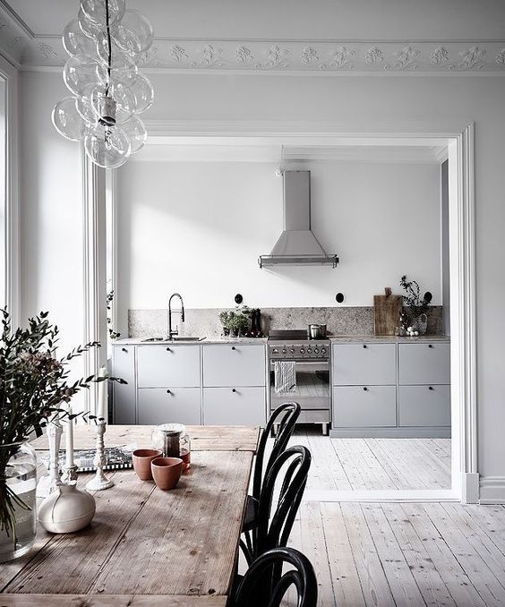 a Scandinavian space with white walls and whitewashed floors, grey cabinets, a wooden table and black chairs