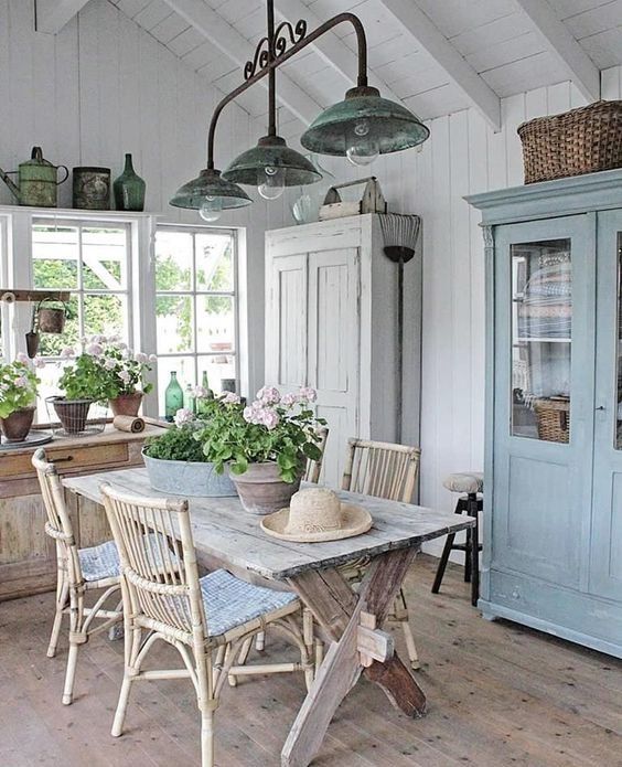 a beautiful Scandinavian veranda with a whitewashed and blue cupboard, with a whitewashed table and rattan chairs, with potted blooms and greenery